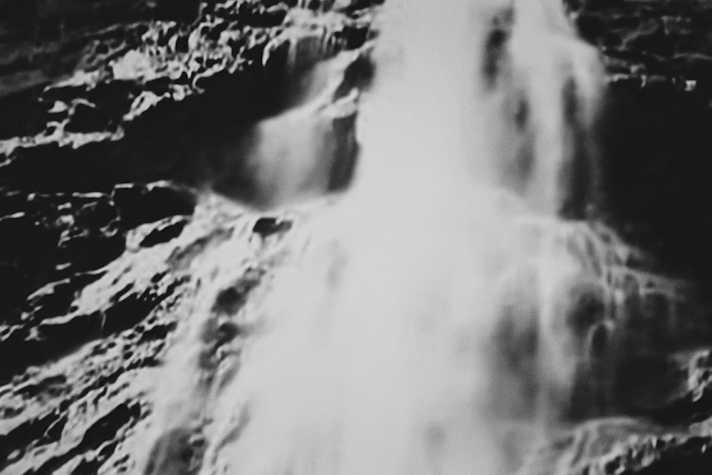 A black and white still featuring water pouring in front of a textured rocky surface