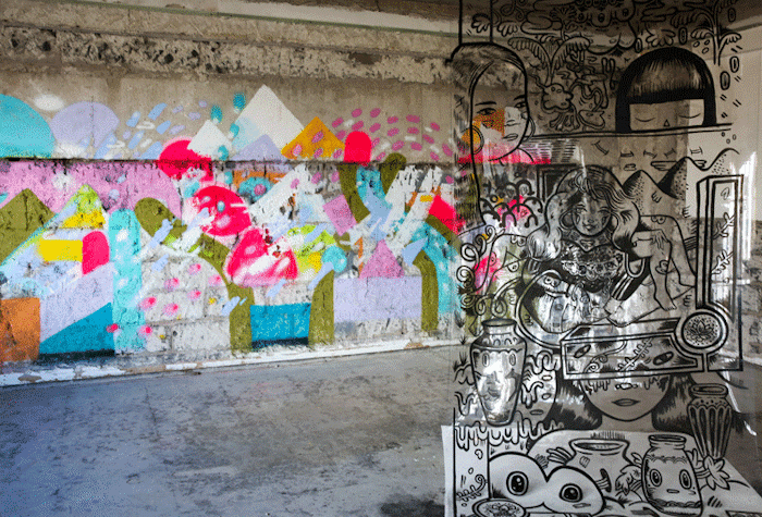 A glass wall to the right has black drawings and you can see behind a wall of concrete with colorful grafitti and painting.