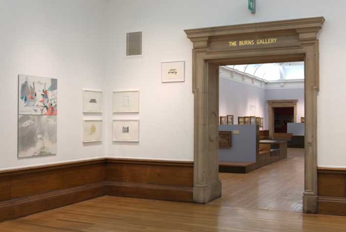 room in the kelvingrove gallery. on the left there are works hung on the wall. on the right is a large stone arch which reads 'the burns gallery' leading to another room.