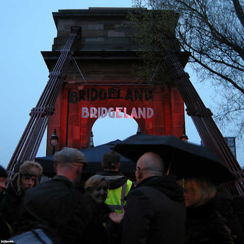 group of people stood on a bridge. on the bridge there is a sign that says bridgeland.