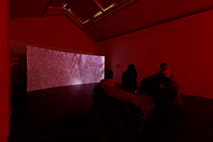 Installation view, people viewing film screen draped across the gallery space