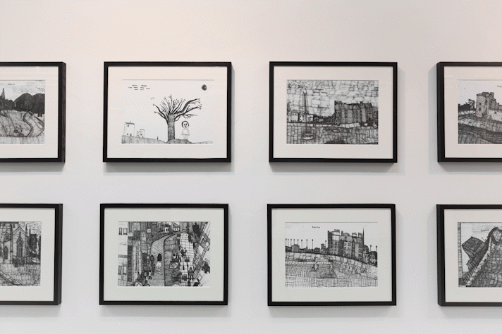 eight intricate pen drawings in black frames hang on a white wall