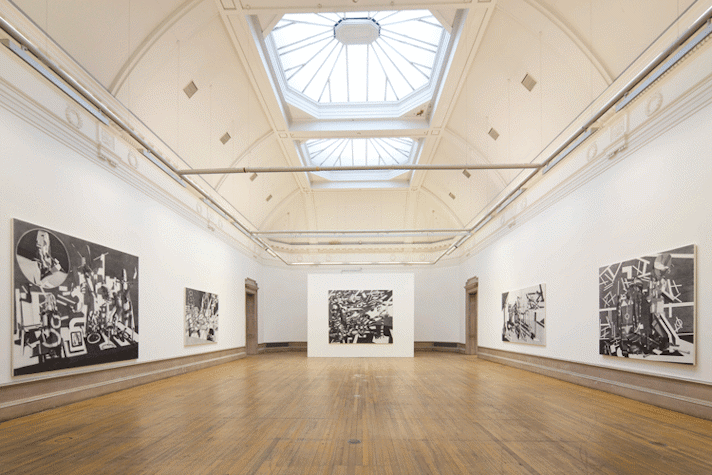 In a long long hallway, with wooden flooring and high ceiling, there are five large monochromatic artworks. Four of them are hung on the wall and one is placed at the end of the hall, put up on a temporary wall, placed ahead of the two doors at the end of the hall.