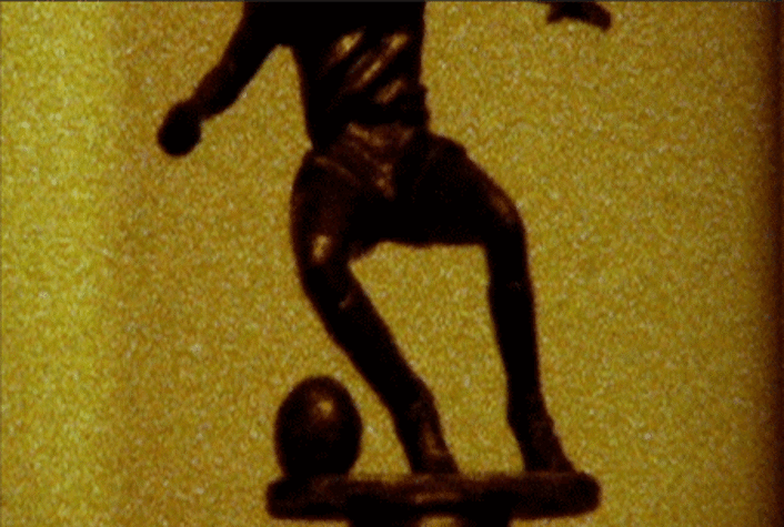 film still, half statue of a person in action about to kick a ball