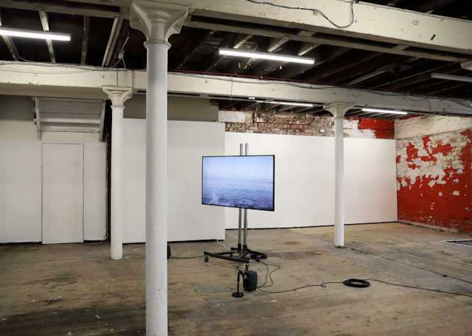 An installation of Yuko Mohri's work in the Pipe Factory, Glasgow. There is a tv screen on a stand. The screen shows an image of the ocean.