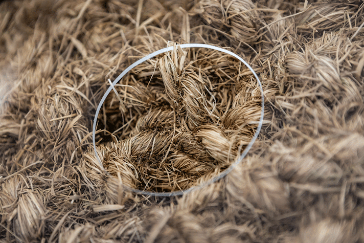 A see-through plastic surface with a circle hole in it, within which there is frayed rope-like material.