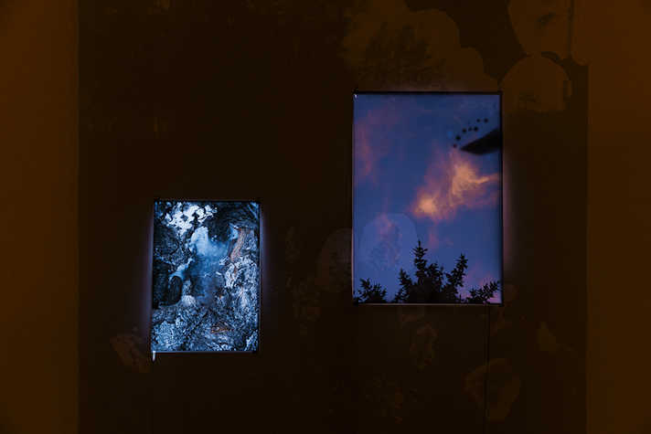 In a dark room, two large lit artworks are presented next to each other.