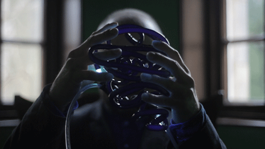 A man is holding a tubular sculpture in his hands, there is a light at the end of it.