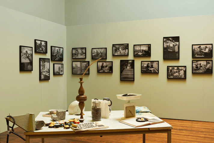 unusual objects sit on a table. black and white photos are mounted on a green wall behind