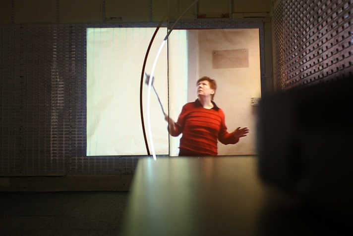 projection in a room. in the projection there is a person wearing red looking up and to the side.
