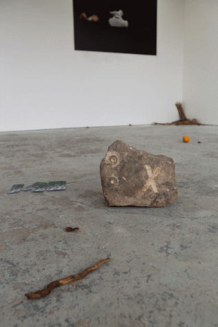 a rock with an 'x' carved into it sits on a gallery floor