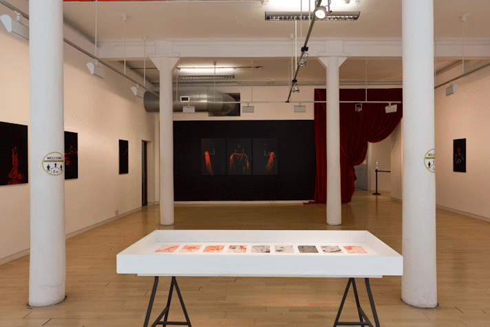 a vitrine holds a series of abstract prints in grey and orange