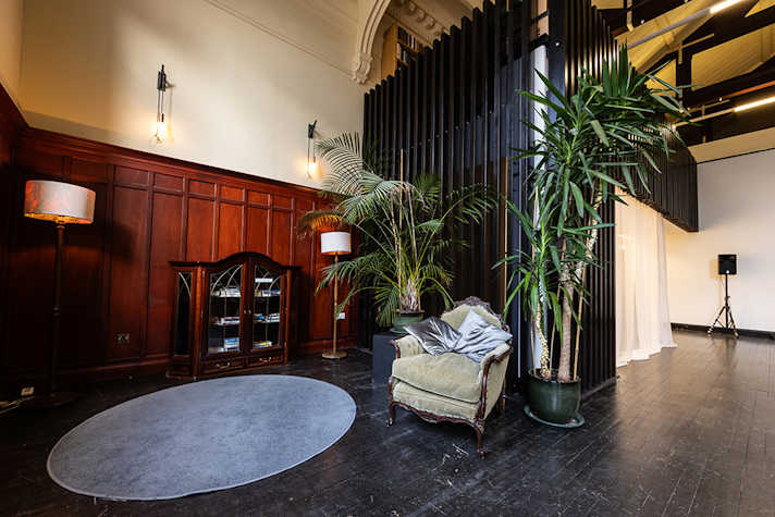 An panelled room with an armchair surrounded by large plants. There is a light rug on the ground.