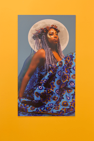 portrait photograph of a person of colour on bright blue background with flowers in their hair and moon behind their head like a halo