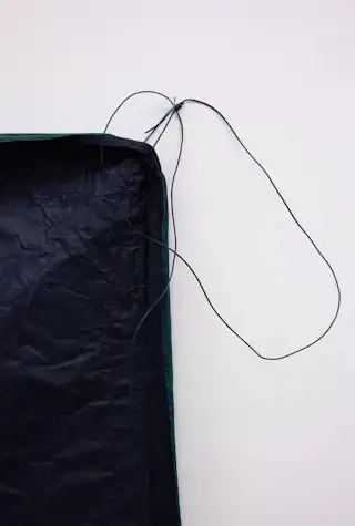 Close up of an abstract wall-mounted sculpture made of a waterproof-looking black fabric, cord attaches the corner of the sculpture to a pin on the wall.