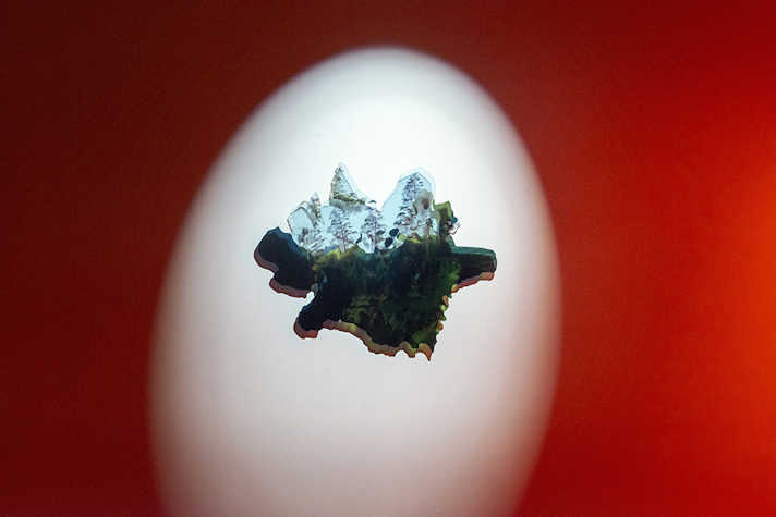 exhibition image of randomly shaped object on wall with a white spotlight surrounded by a red glow