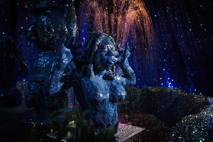 A ceramic figure of a nude woman with water spraying behind, surrounded in blue sparkly material.