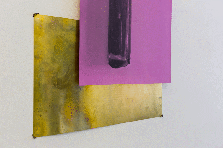 close up of an artwork with a sheet of brass and pink paper with black abstract print