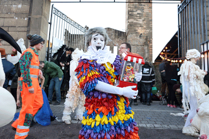 Performers dressed in circus costume in front of a large gate
