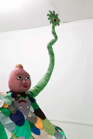 image of a large scale surreal sculpture with 5 baby-like heads, wiggling arms and a patchwork of fabric cut outs laid over it in the shape of cartoon-like arms and faces