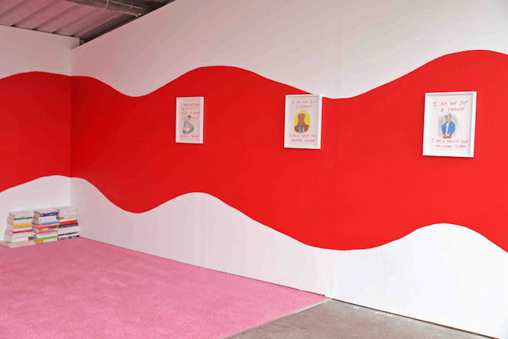 a wide red squiggle painted on a gallery wall. Small framed drawings hung on the wall. A pink carpet and pile of books