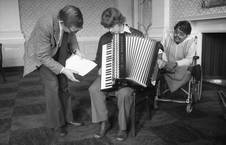 A black and white image featuring three people in the centre.