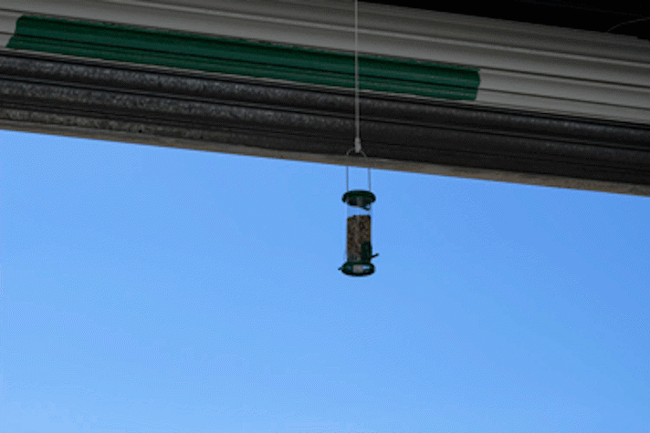 a bird feeder hangs from the ceiling of a gallery. One side of the gallery is open to the outside.
