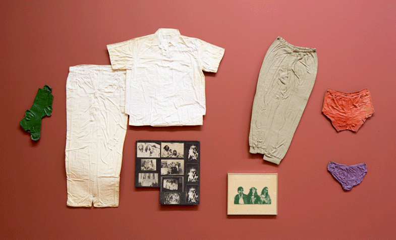 Multiple object sa re hung on the wall. There are two pants, a shirt, underwear and sock, which all look crushed, stuck to the wall. There are two pictures, one is a collage of black and white images of three people. There is a framed picture of the same three people in the colour green.