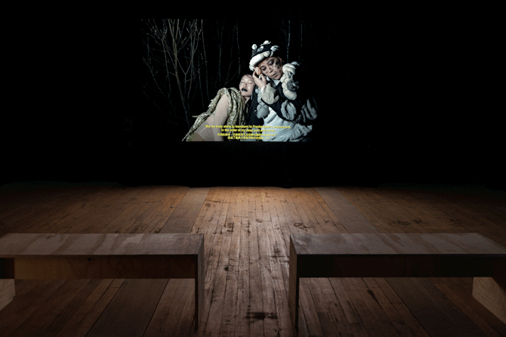 Film is projected onto a screen in a dark room. There are wooden benches facing the screen.