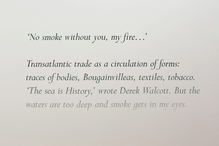 black cursive text on a gallery wall that fades to a light grey reads 'No smoke without you, my fire...', 'Transatlantic trade as a circulation of form: traces of bodies, Bouganvilleas, textiles, tobacco. 'The Sea is history' wrote Derek Walcott. But the waters are too deep and smoke gets in my eyes.'