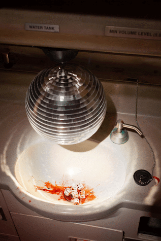 Detail of Jenkin van Zyl installation at Tramway. A discoball hangs over an aeroplane sink unit. There are dice in the sink and a pool of blood.