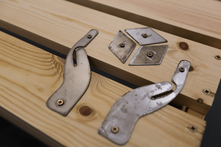 detail of metal symbols screwed to a wooden structure. the symbols show two hands and a small box floating between them