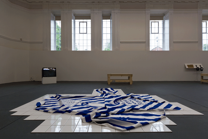 a blue and white piece of striped fabric with printed lettering lost in folds sits on a section of white tiled floor
