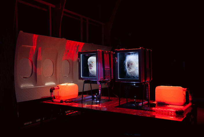 An image of jenkin van zyl's installation. There are 2 fridges holding mangled heads, panels from an aeroplane and eerie red lighting.