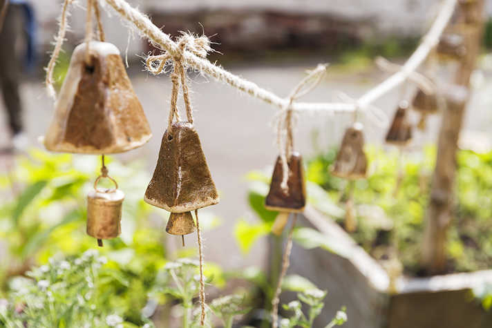 A close up of a string of bells that are hanging over green plants.