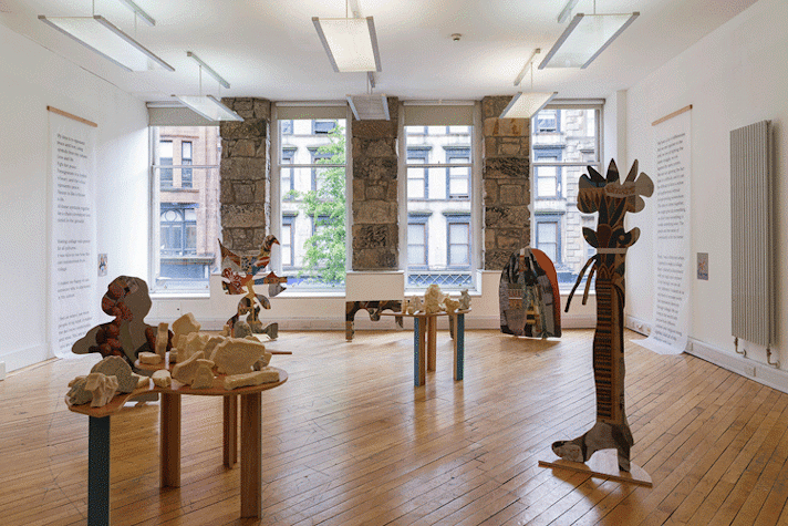 Artwork is displayed on tables and standing alone on a wooden floor.