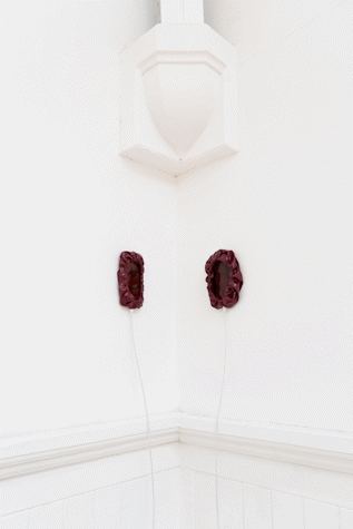 two iphones are mounted on two adjacent white walls. They sit inside burgundy PVC covers that are gathered at their edges around the phone screens