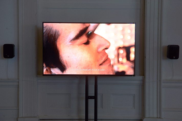 In front of a white wall a screen with a film showing (a close-up of a man closing his eyes) as part of an art installation in the Gallery of Modern Art, Glasgow International 2018.