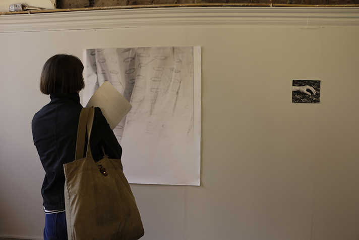 Gallery installation, hung print and photograph showing a hand, festival attendee viewing the work