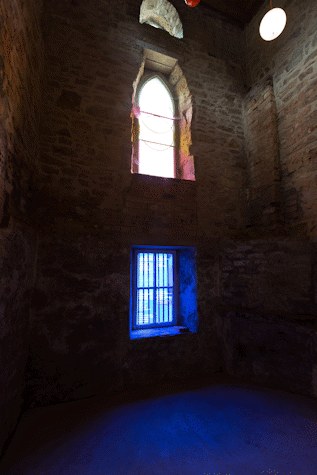 a chapel-like double height space in an old building. The bottom window has a blue film over the panes, the blue light glows onto the bricks around