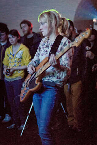 woman playing a bass guitar with an audience stood behind her.