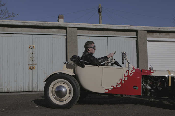 Person sitting in a custom made car in front of some garages