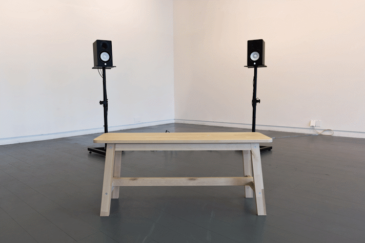 a bench sits in front of two speakers on stands