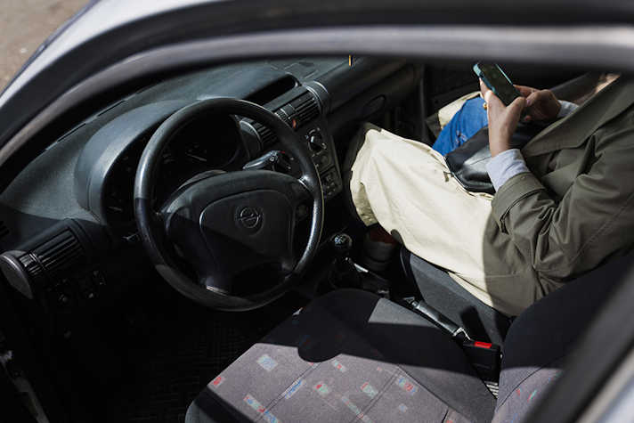 The open door into the driver's seat of a silver car. There is a person sitting in the passenger seat, their face is obscured.