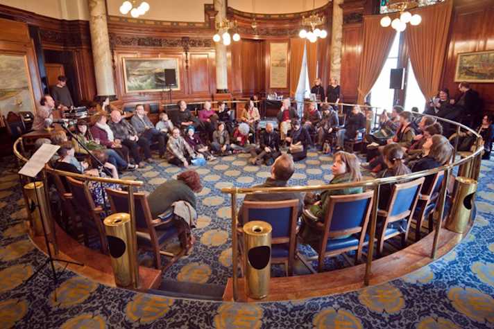 group of people sitting in a circular forum in an ornate meeting room