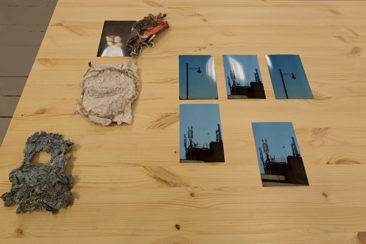 photographs of a blue sky and silhouetted streetlamps sit with pieces of crumpled paper on a wooden table