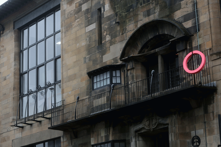 A pink ring like structure is hanging on the railing of an old building.