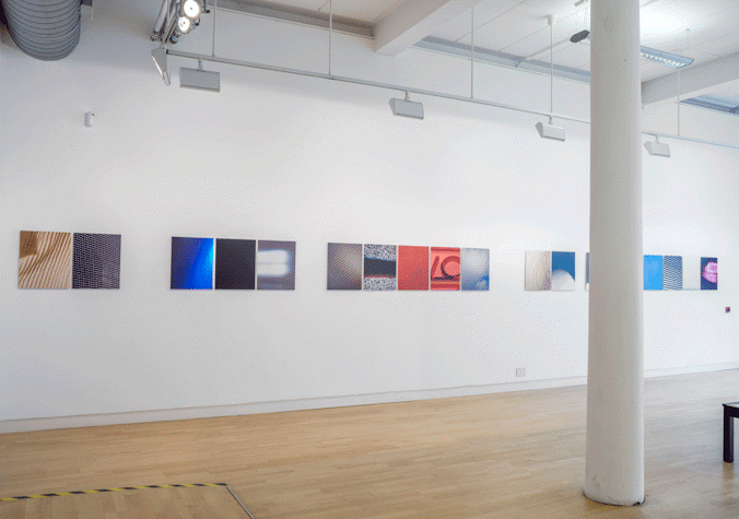 In a straight line, there are multiple artworks placed on a blank wall. They all have different colours. They are all the same size.