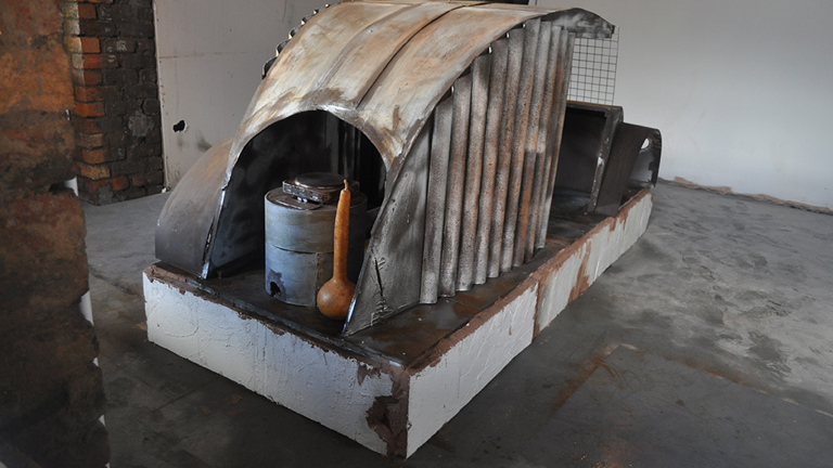 Installation view of a sculpture made from scrap metal in the form of a shelter of some kind
