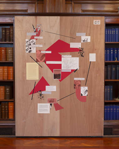 A large piece of MDF with images and writing on it, against bookcases.